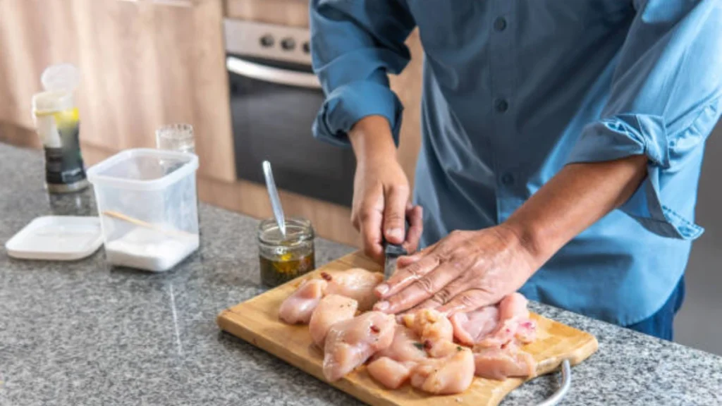 Raw chicken breasts being seasoned with salt, pepper, garlic powder, and herbs on a wooden cutting board, ready for cooking