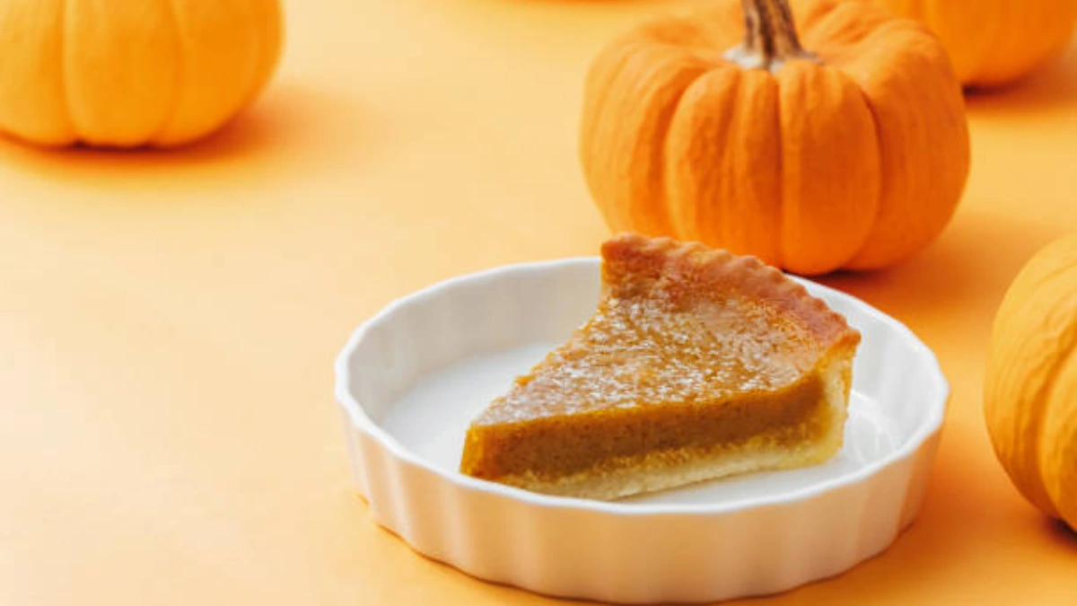 A beautifully styled pumpkin pie on a rustic wooden table, surrounded by autumn decorations like fallen leaves, small pumpkins, and cinnamon sticks, with a golden crust and a creamy filling.