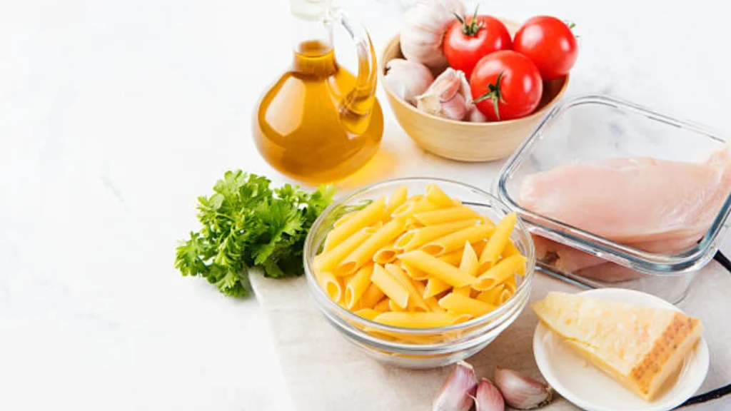 A spread of ingredients for garlic parmesan chicken pasta, including chicken breasts, pasta, garlic, parmesan cheese, butter, and seasonings, ready to be added to the crock pot.